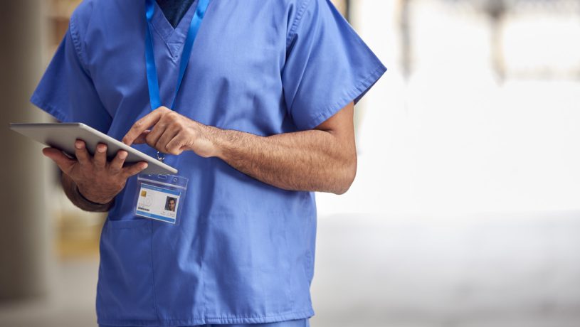 Close Up Of Male Medical Worker In Scrubs With Digital Tablet In Hospital.